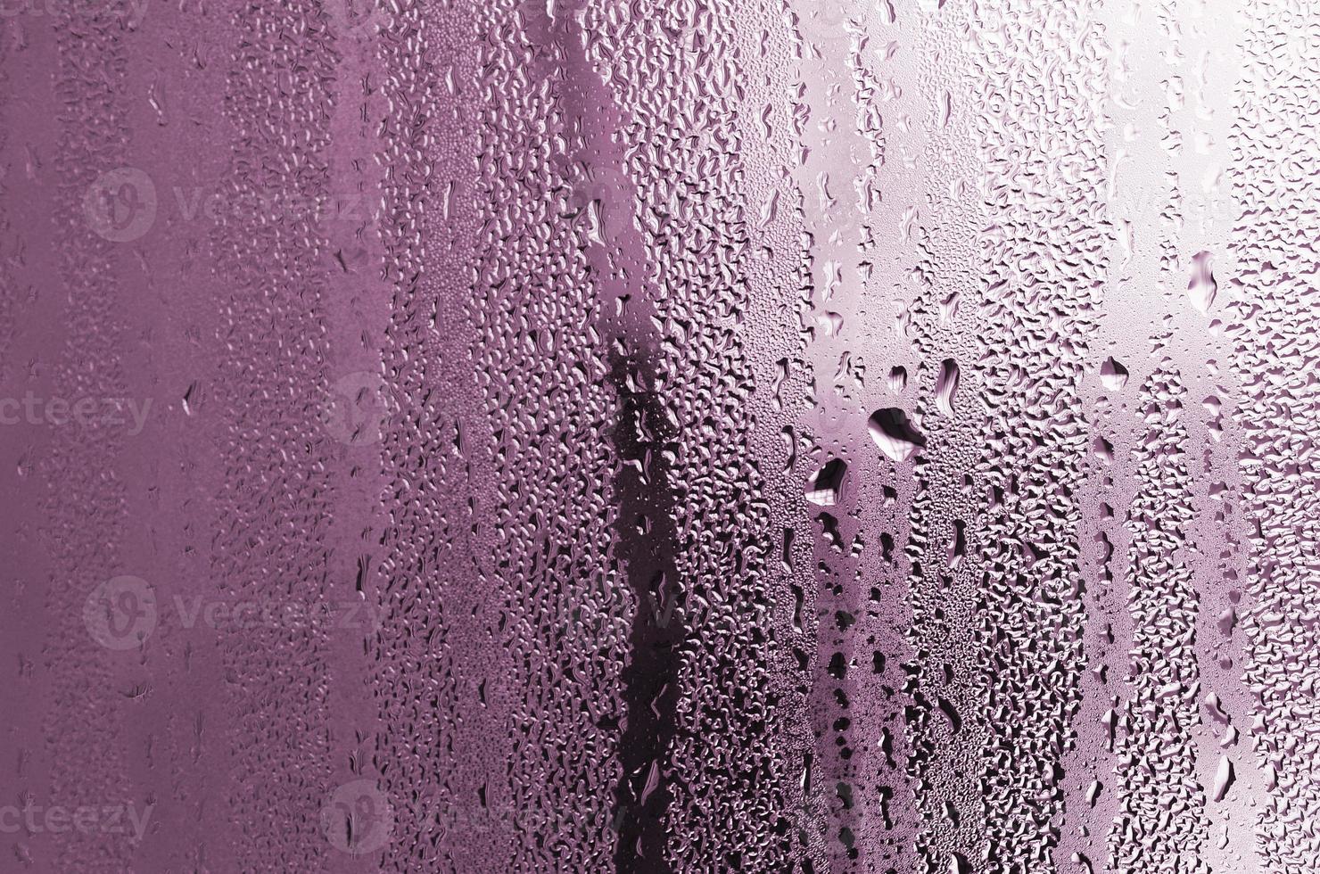 textura de una gota de lluvia sobre un fondo transparente húmedo de vidrio. tonificado en color rosa foto