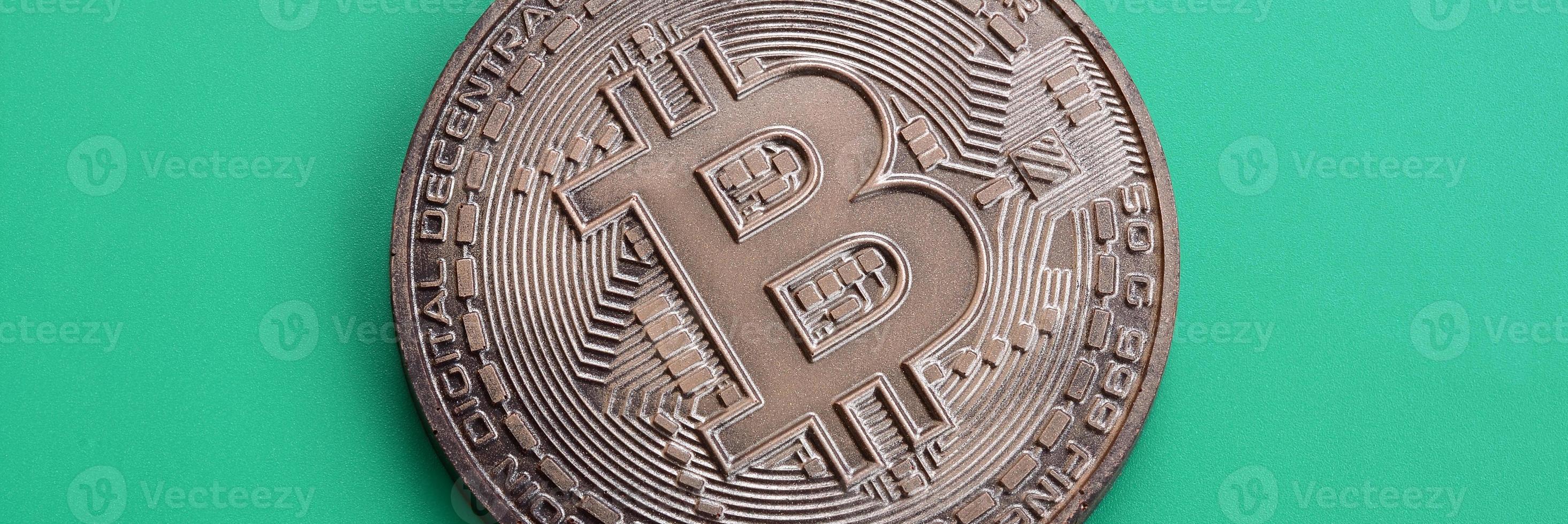 Chocolate product in the form of physical bitcoin lies on a green plastic background. Model of the crypto currency in the edible form photo