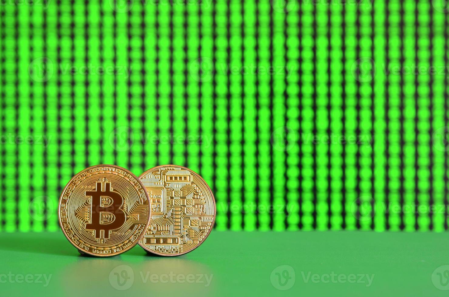 Two gold bitcoins lie on the green surface on the background of the display, which shows the process of mining the crypto currency photo