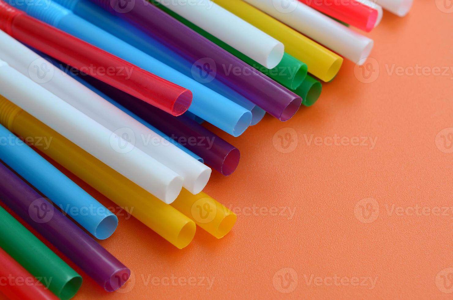 Many colorful straws for drinks lies on a bright orange background surface photo