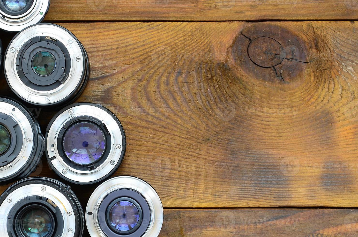 Several photographic lenses lie on a brown wooden background. Space for text photo
