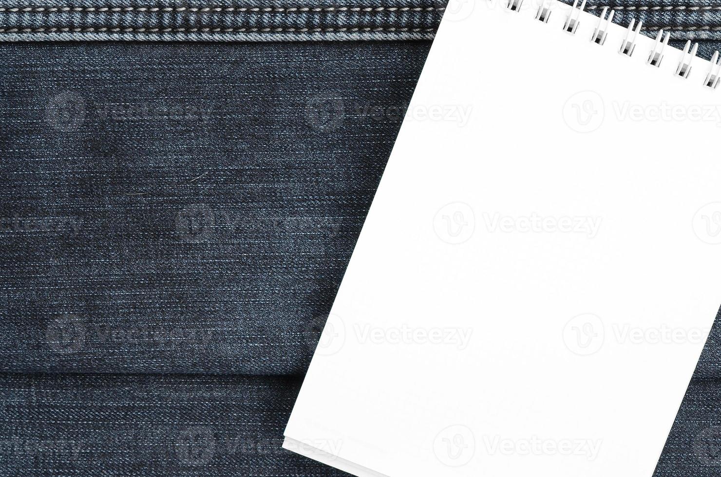 White notebook with clean pages lying on dark blue jeans background. Image with copy space photo