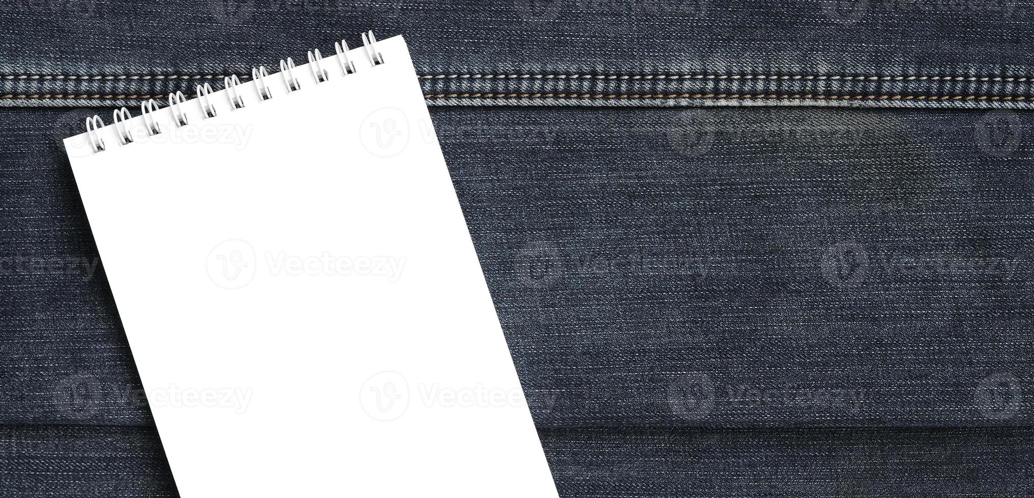 White notebook with clean pages lying on dark blue jeans background. Image with copy space photo