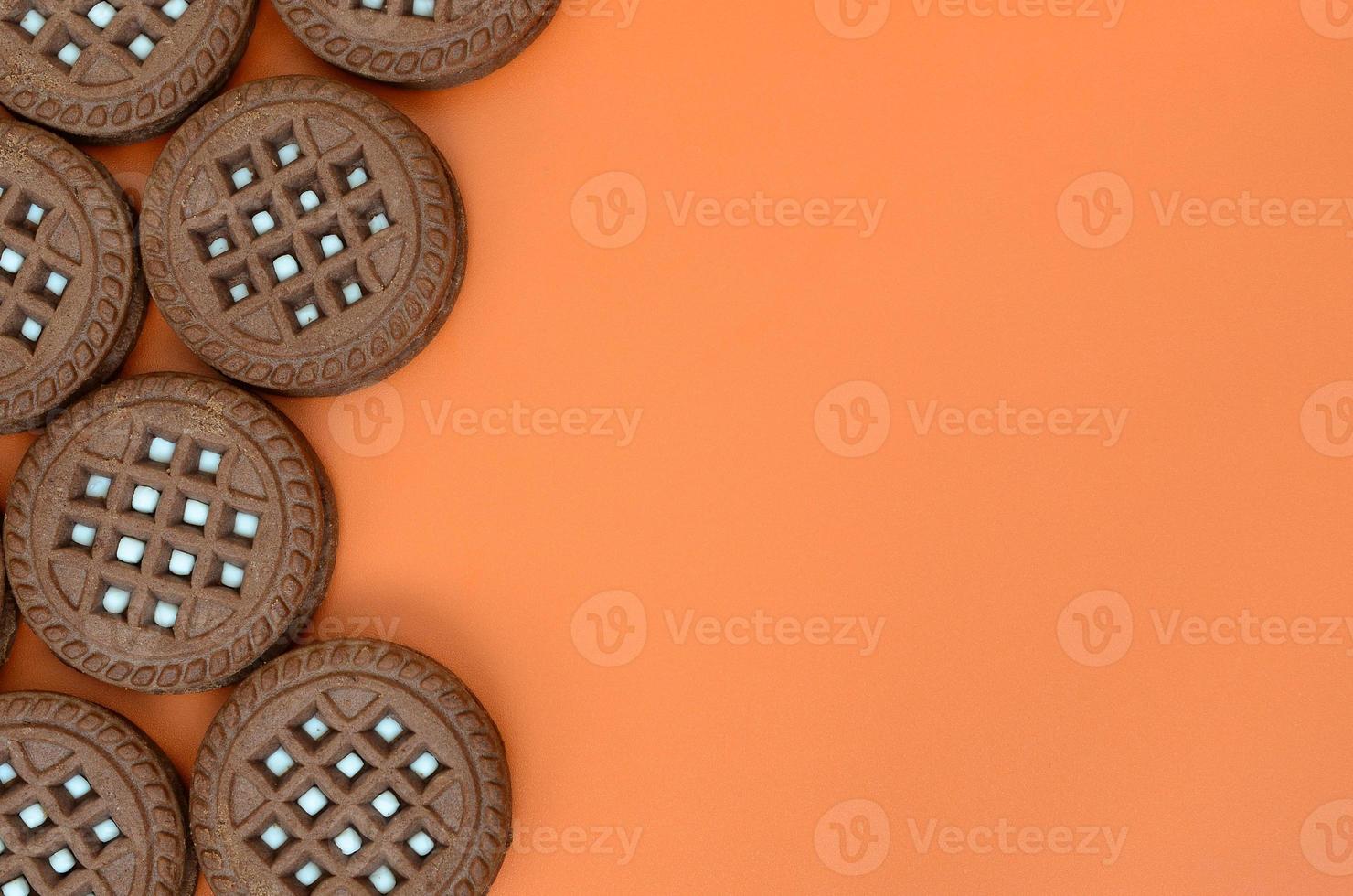 Detailed picture of dark brown round sandwich cookies with coconut filling on an orange surface. Background image of a close-up of several treats for tea photo