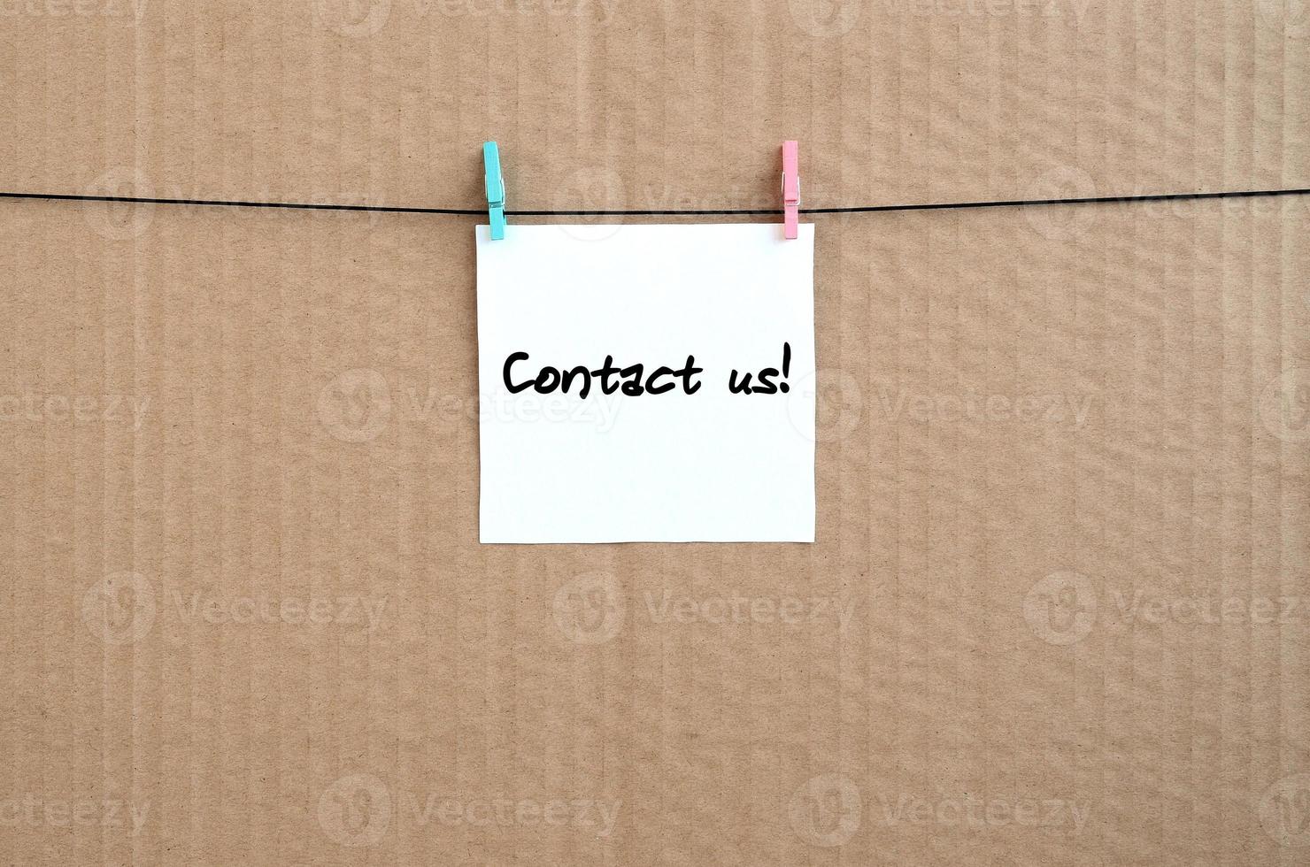 Contact us Note is written on a white sticker that hangs with a clothespin on a rope on a background of brown cardboard photo