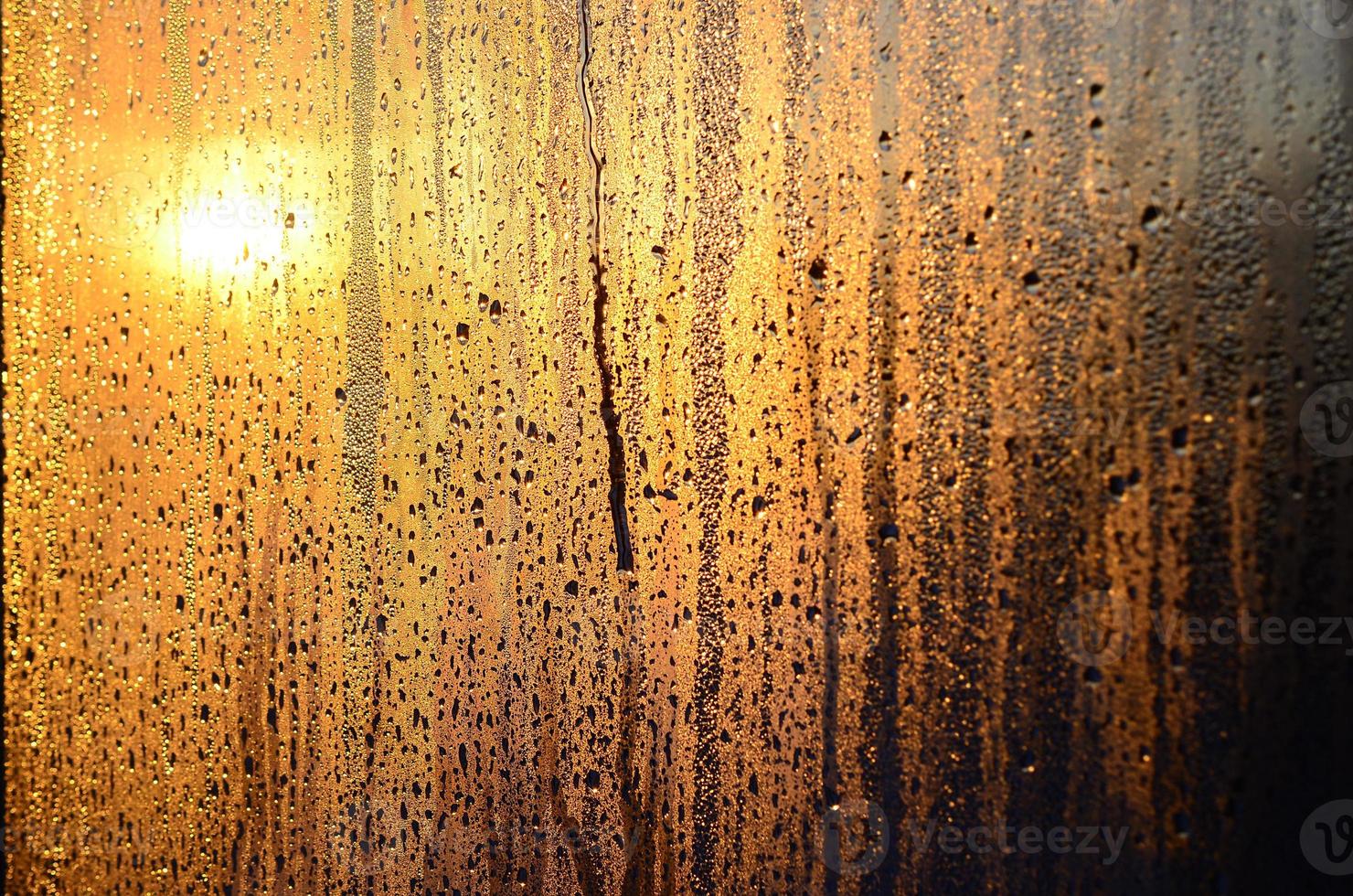 The texture of misted glass with a lot of drops and drips of condensation against the sunlight at dawn. Background image photo