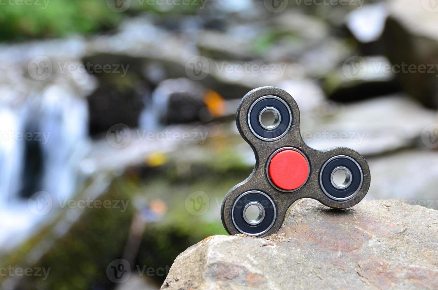 The wooden spinner lies on the rocks against the background of a small waterfall and a river photo