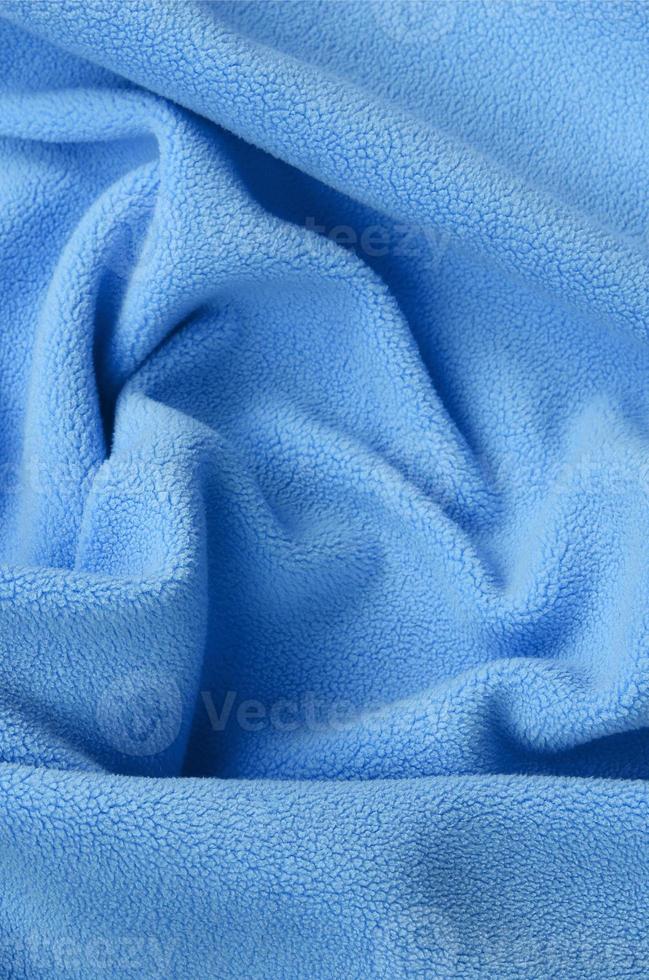 The blanket of furry blue fleece fabric. A background of light blue soft plush fleece material with a lot of relief folds photo