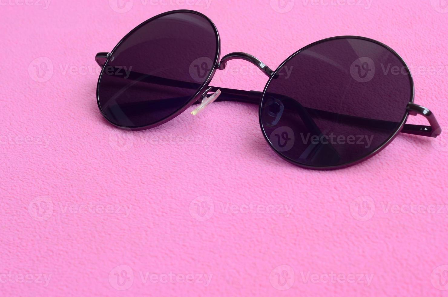 Stylish black sunglasses with round glasses lies on a blanket made of soft and fluffy light pink fleece fabric. Fashionable background picture in female colors photo