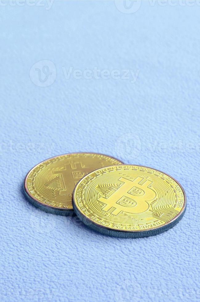 Two golden bitcoins lies on a blanket made of soft and fluffy light blue fleece fabric. Physical visualization of virtual crypto currency photo