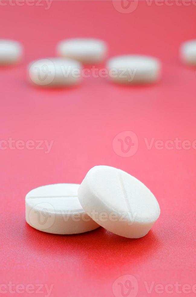 A few white tablets lie on a bright red background surface. Background image on medical and pharmaceutical topics photo