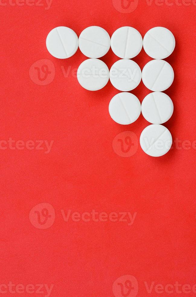 Several white tablets lie on a bright red background in the form of a triangular arrow. Background image on medicine and pharmaceutical topics photo