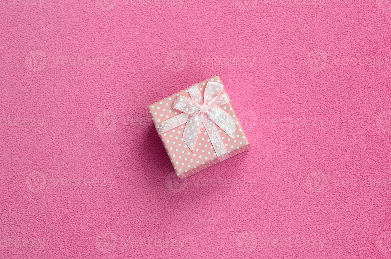 A small gift box in pink with a small bow lies on a blanket of soft and furry light pink fleece fabric. Packing for a gift to your lovely girlfriend photo