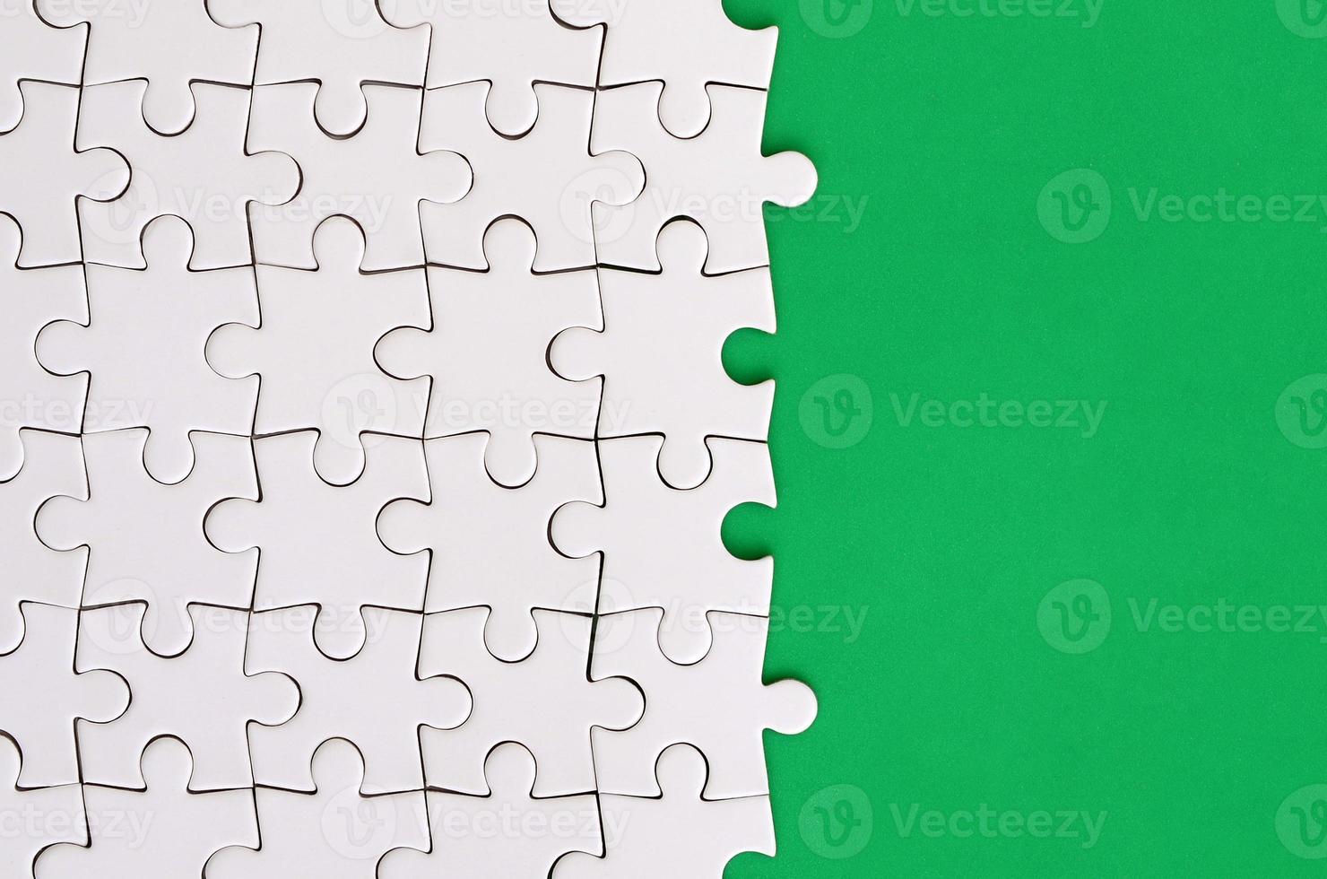 Fragment of a folded white jigsaw puzzle on the background of a green plastic surface. Texture photo with copy space for text