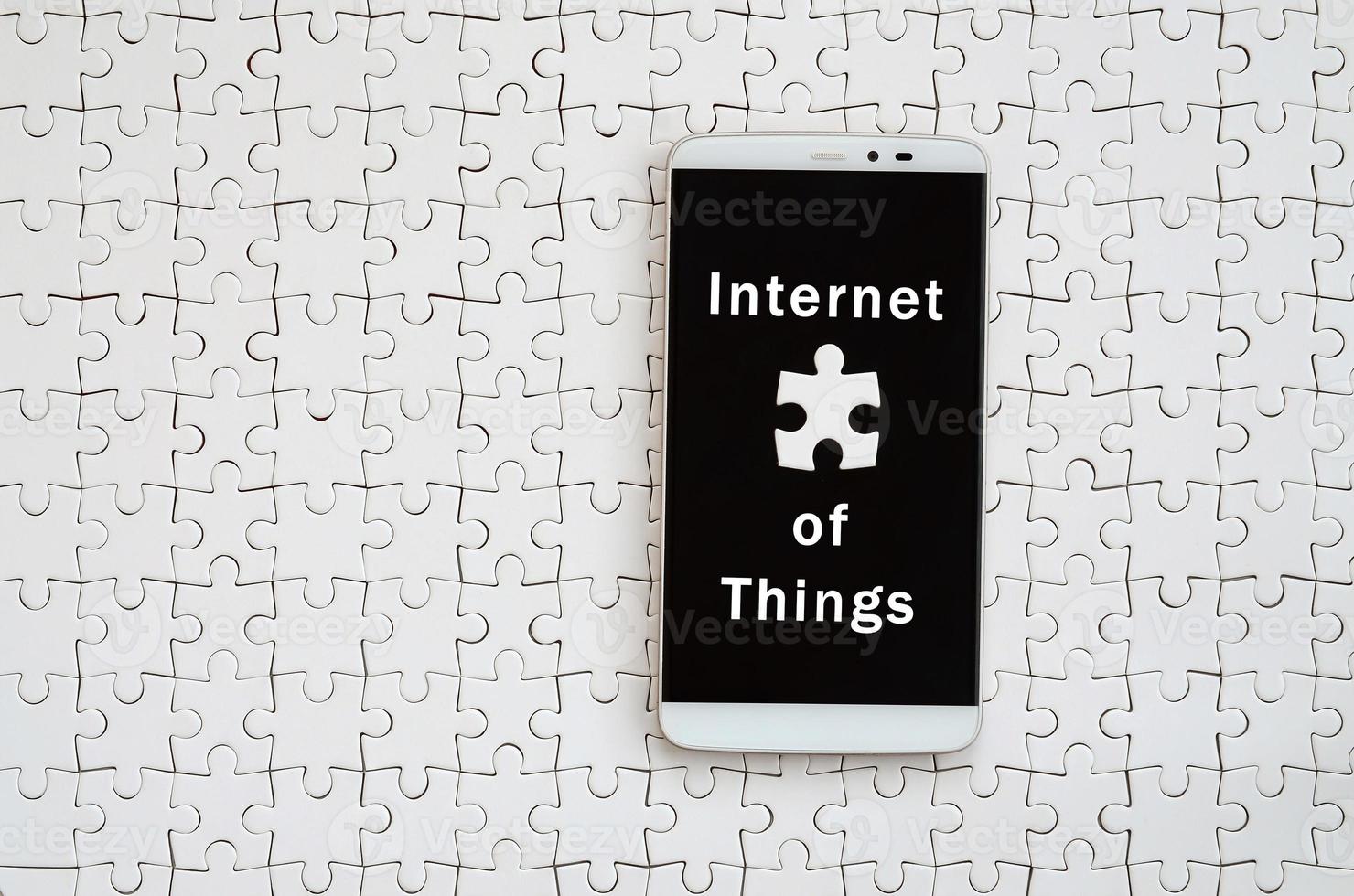 A modern big smartphone with a touch screen lies on a white jigsaw puzzle in an assembled state with inscription. Internet of things photo