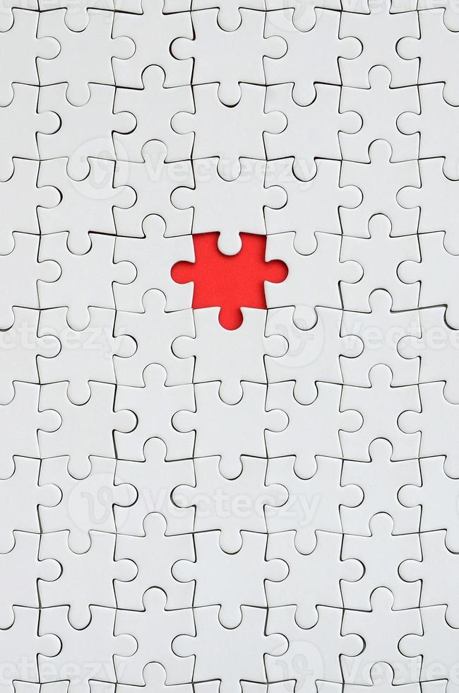 The texture of a white jigsaw puzzle in an assembled state with one missing element forming a red space photo