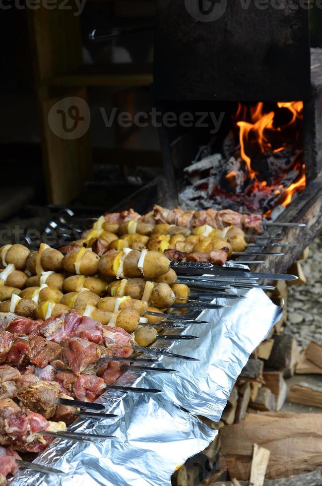 Raw meat and potatoes are planted on metal skewers. The process of cooking shish kebabs. Russian and Ukrainian camp food photo