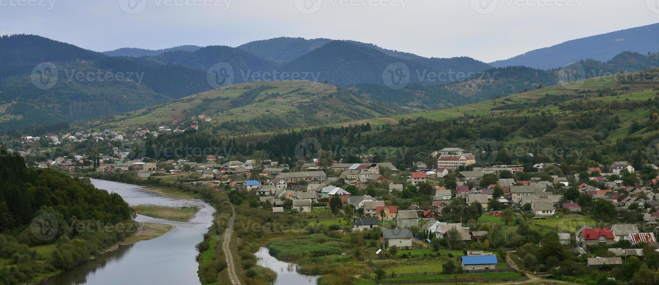 A beautiful view of the village of Mezhgorye, Carpathian region. A lot of residential buildings surrounded by high forest mountains and long river photo