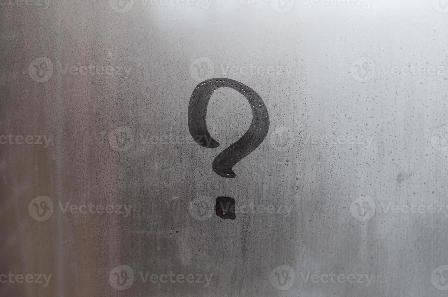 The inscription on glass, question mark concept. Question sign is painted on the surface of misted and wet window photo