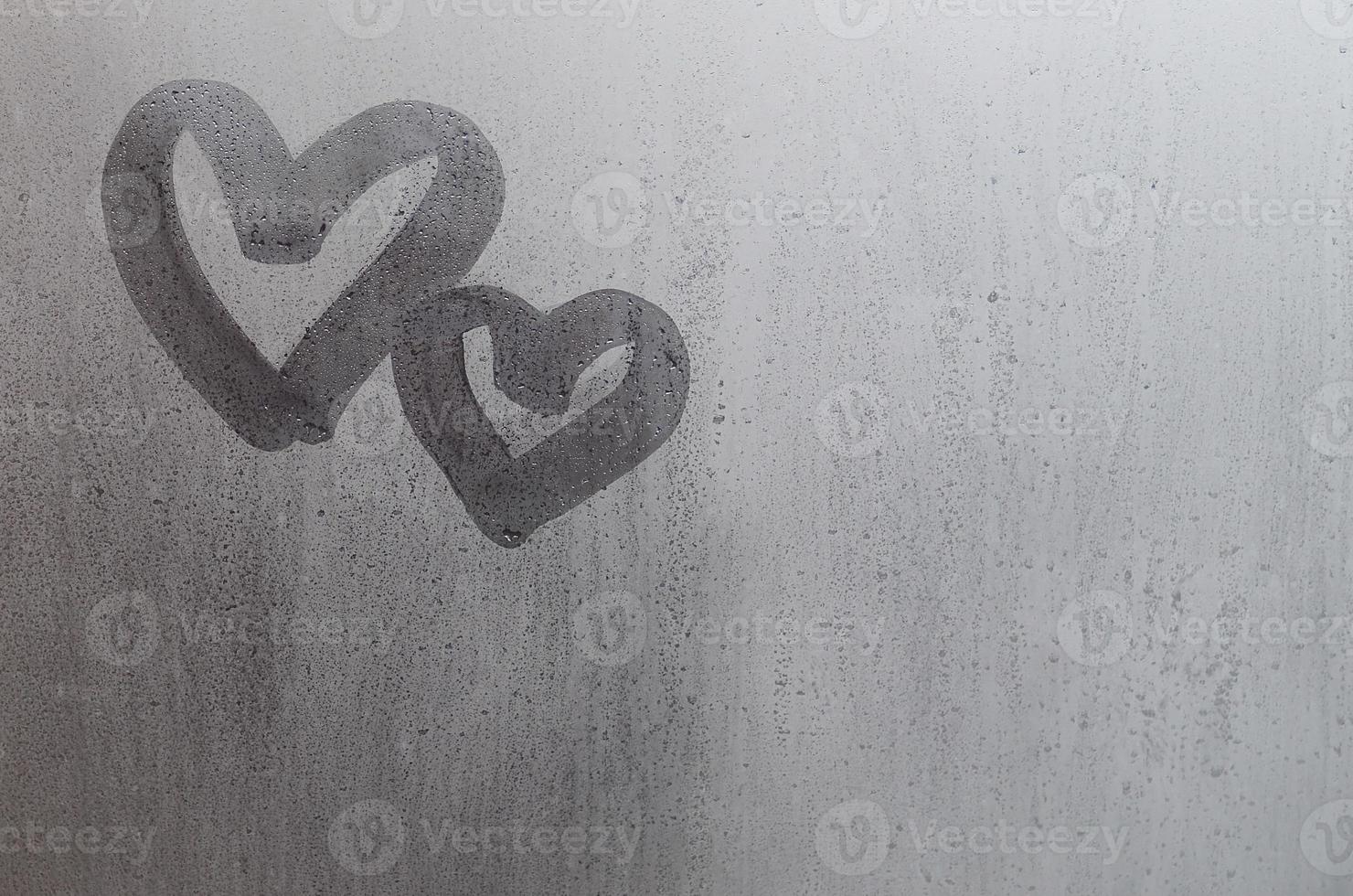 Couple of abstract blurred love heart symbol drawn by hand on the wet window glass with sunlight background. Template for Valentine Day postcards photo