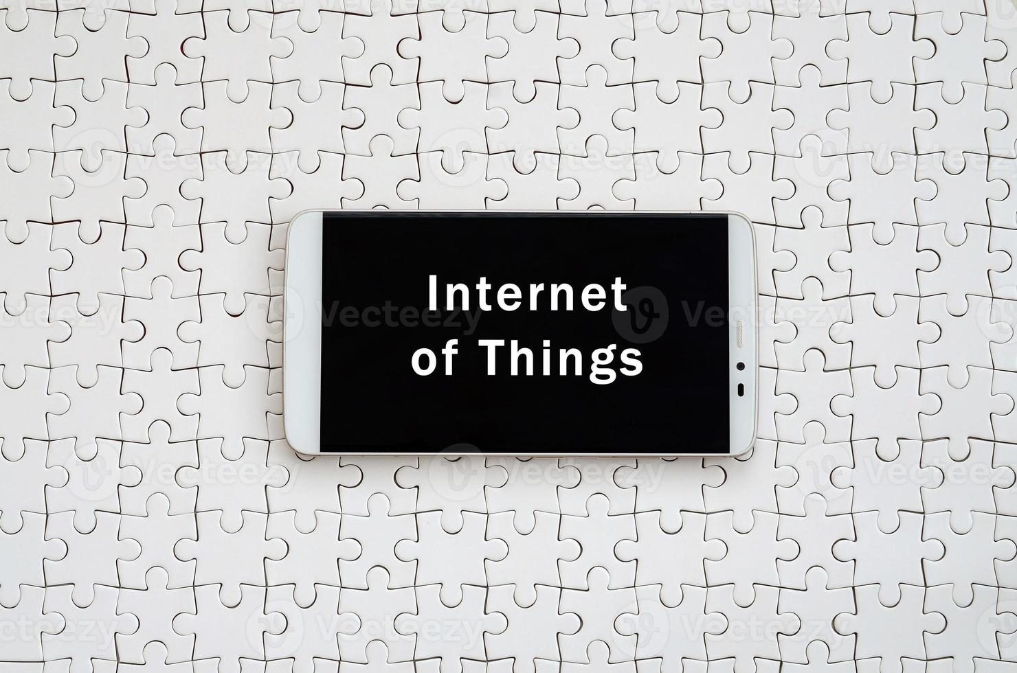 A modern big smartphone with a touch screen lies on a white jigsaw puzzle in an assembled state with inscription. Internet of Things photo