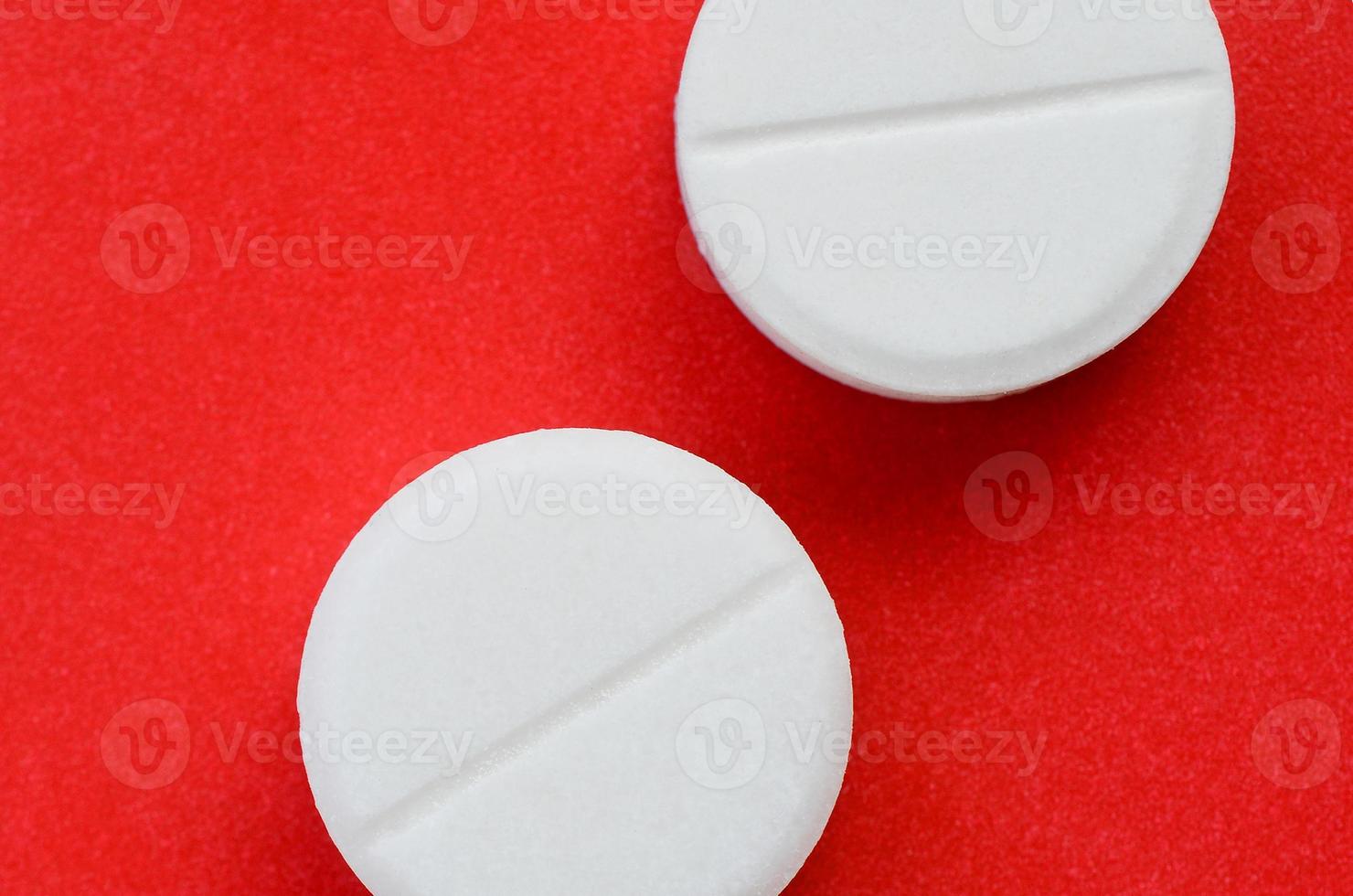 A few white tablets lie on a bright red background surface. Background image on medical and pharmaceutical topics photo