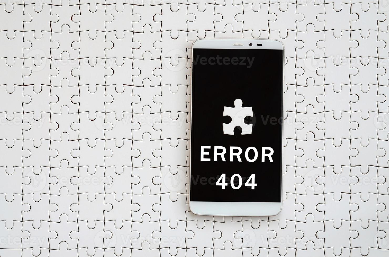 A modern big smartphone with a touch screen lies on a white jigsaw puzzle in an assembled state with inscription. Error 404 photo