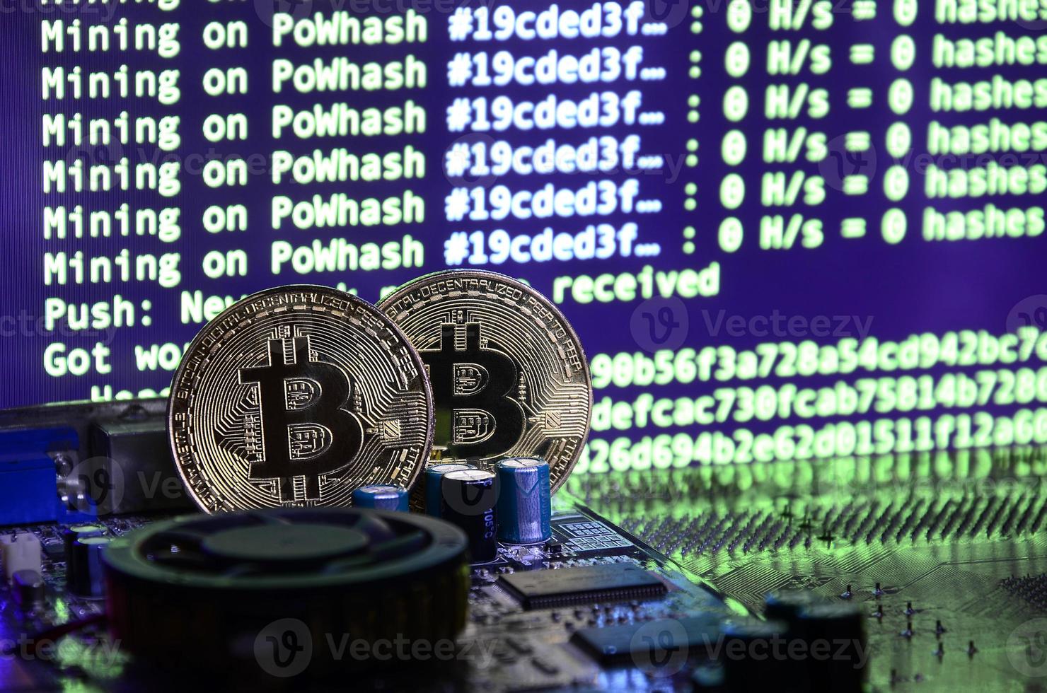 Two bitcoins lies on a videocard surface with background of screen display of cryptocurrency mining by using the GPUs photo