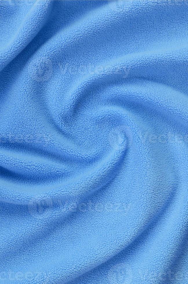 The blanket of furry blue fleece fabric. A background of light blue soft plush fleece material with a lot of relief folds photo