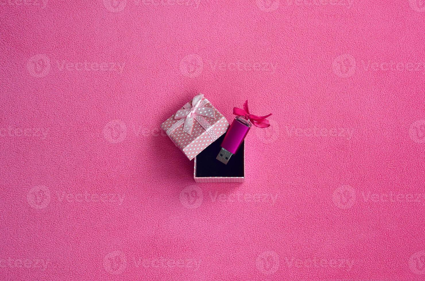 Brilliant pink usb flash memory card with a pink bow lies in a small gift box in pink with a small bow on a blanket of soft and furry light pink fleece fabric. Classic female gift memory card design photo