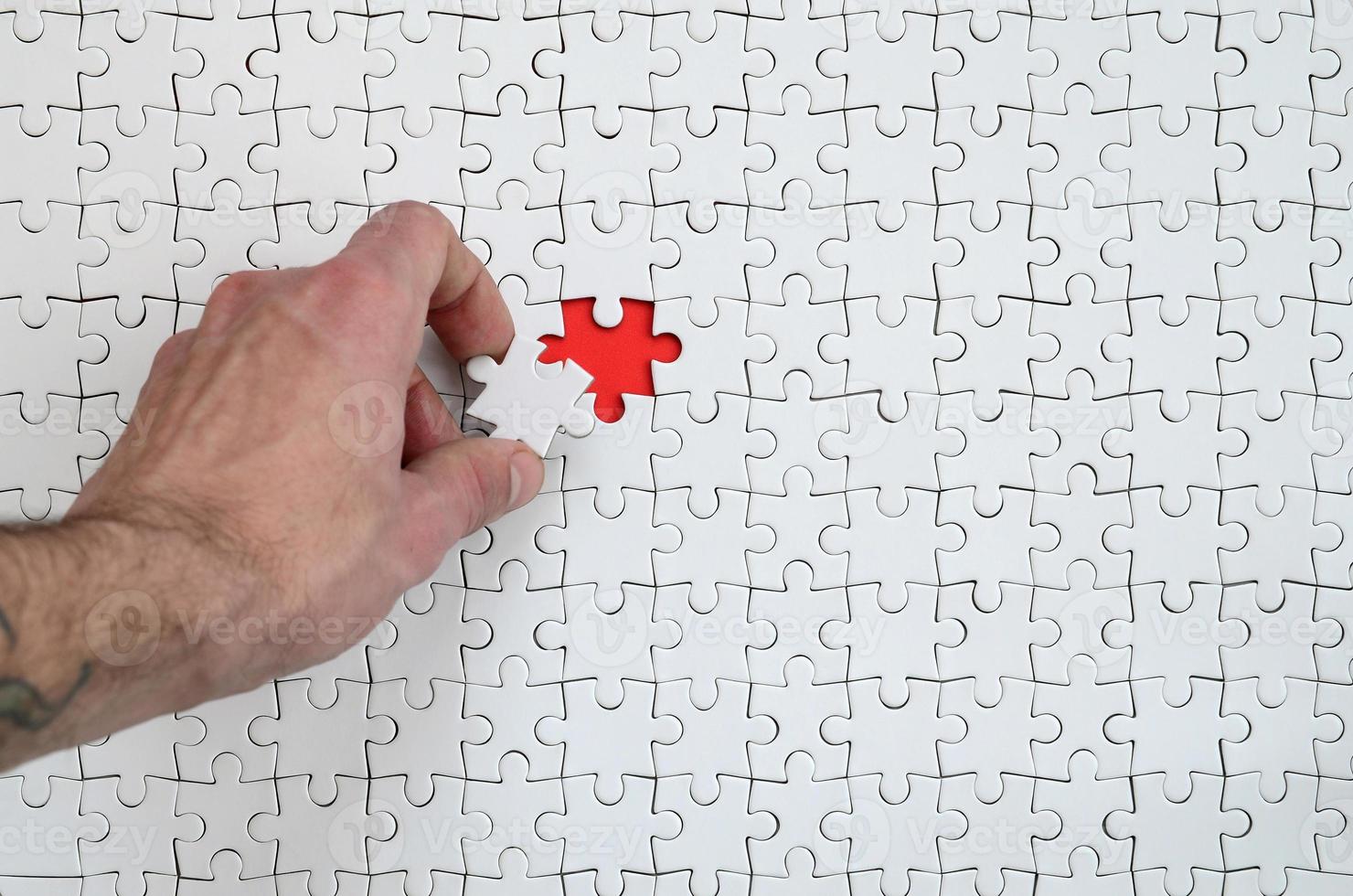 The texture of a white puzzle puzzle in the assembled state with one missing element that the male hand puts in photo