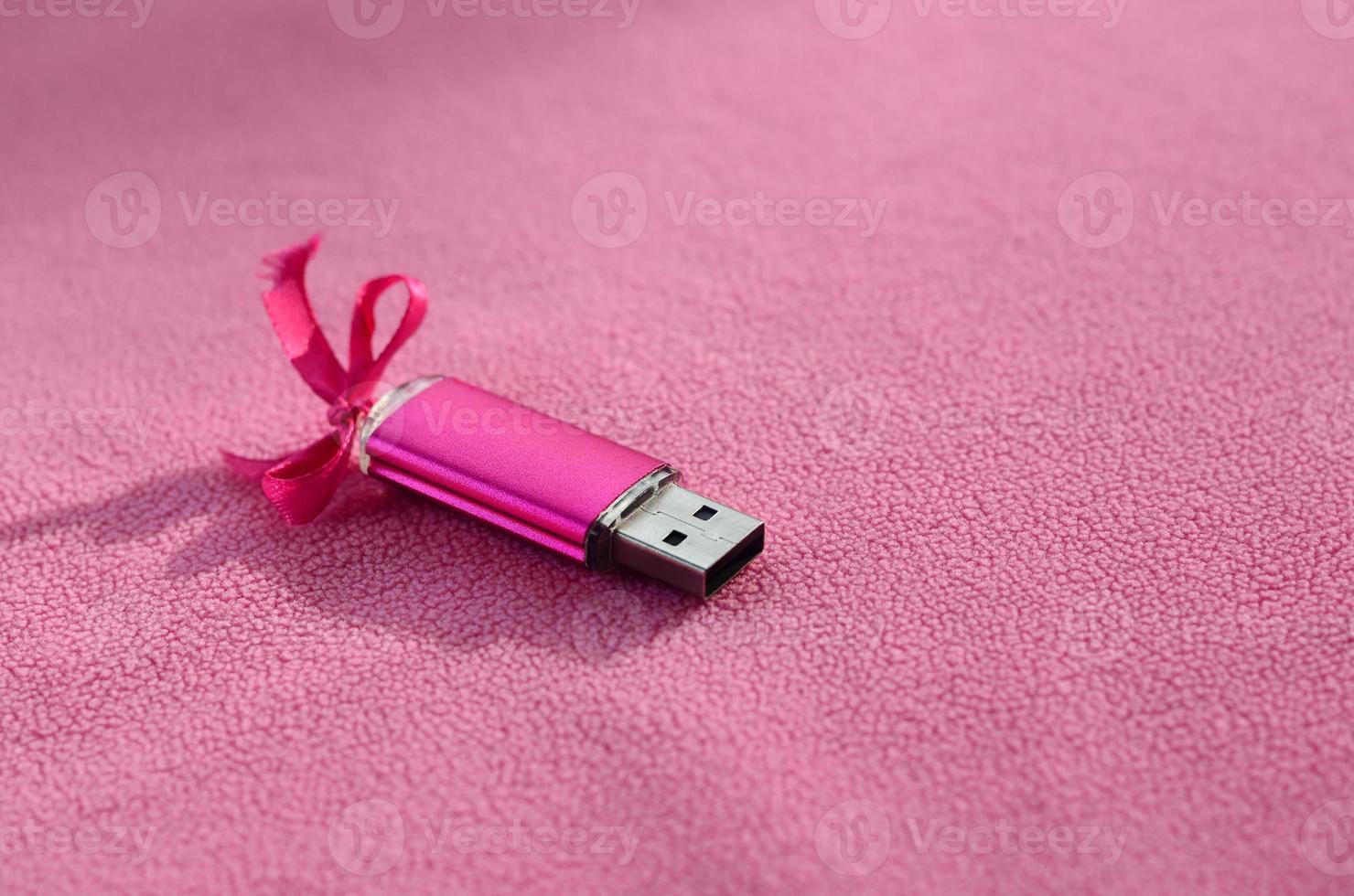 Brilliant pink usb flash memory card with a pink bow lies on a blanket of soft and furry light pink fleece fabric. Classic female gift design for a memory card photo