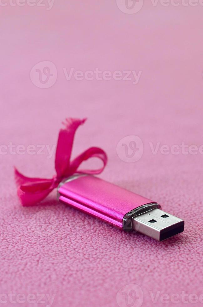 Brilliant pink usb flash memory card with a pink bow lies on a blanket of soft and furry light pink fleece fabric. Classic female gift design for a memory card photo
