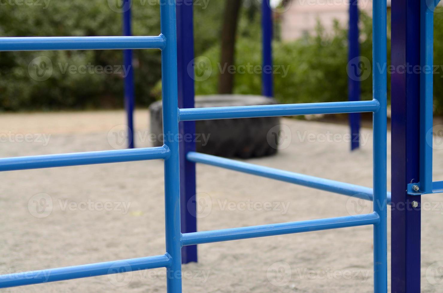Blue metal pipes and cross-bars against a street sports field for training in athletics. Outdoor athletic gym equipment. Macro photo with selective focus and extremely blurred background