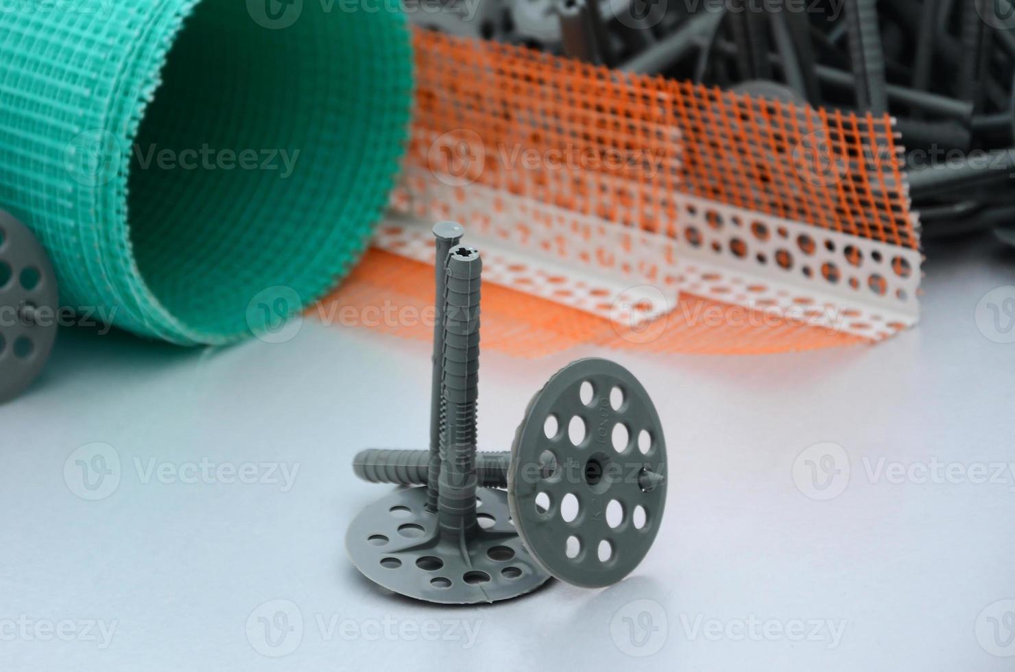 A set of construction items for the insulation of walls. Plastic dowels, a roll of mesh for the insulation of facades and a corner profile with a grid lie on the foam polystyrene surface photo