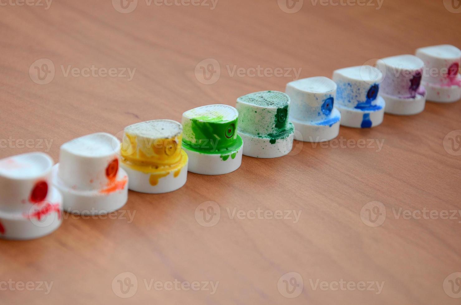 The soiled multicolored nozzles from the paint sprayer are lined up on a wooden table. Street art concept photo