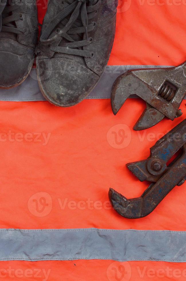Adjustable wrenches and old boots lies on an orange signal worker shirt photo