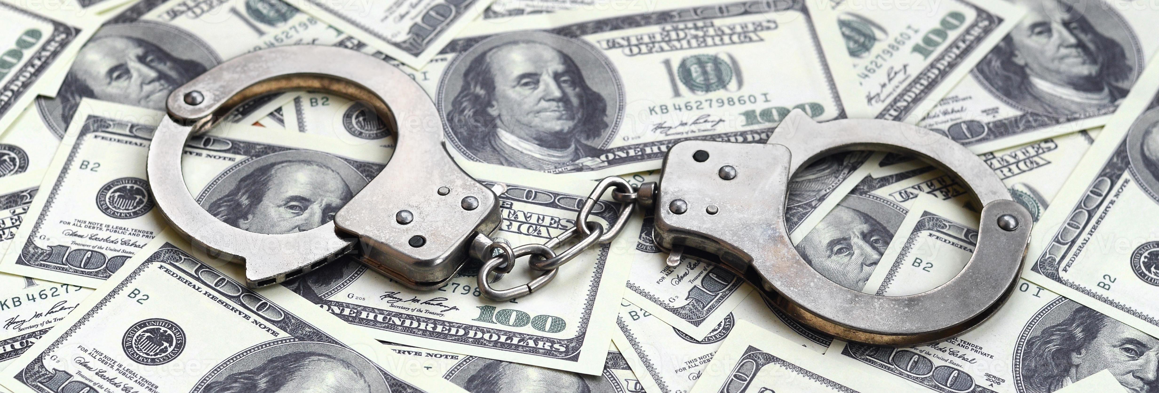 Police handcuffs lie on a lot of dollar bills. The concept of illegal