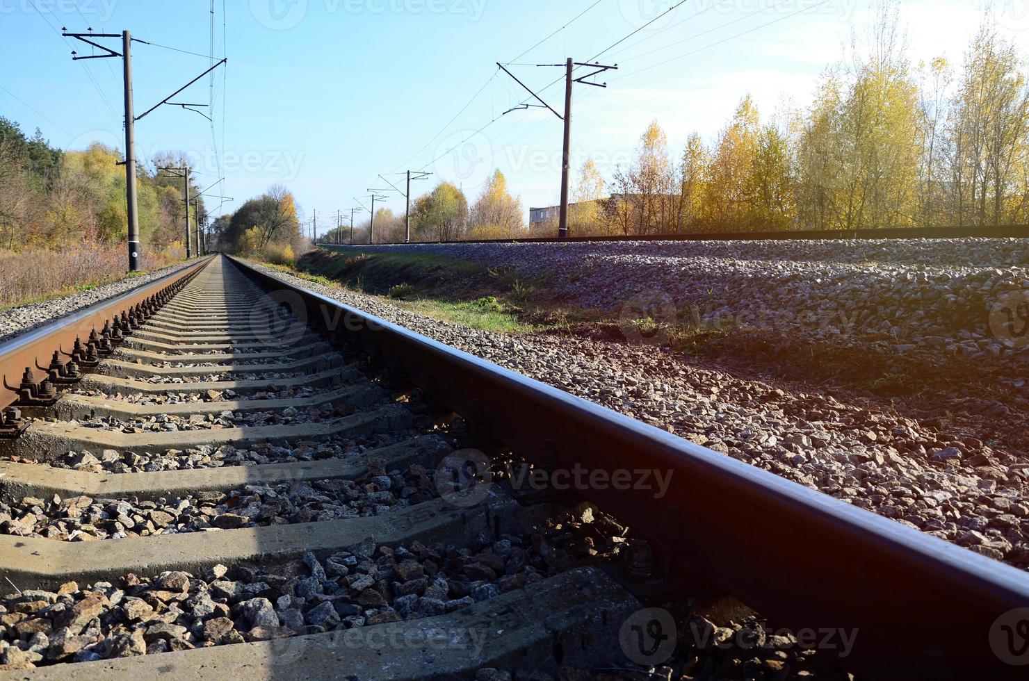 Autumn industrial landscape. Railway receding into the distance among green and yellow autumn trees photo