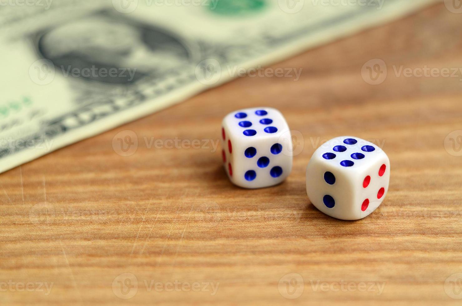 White dice are next to a dollar bill of US dollars on a wooden background. The concept of gambling with rates in monetary units photo