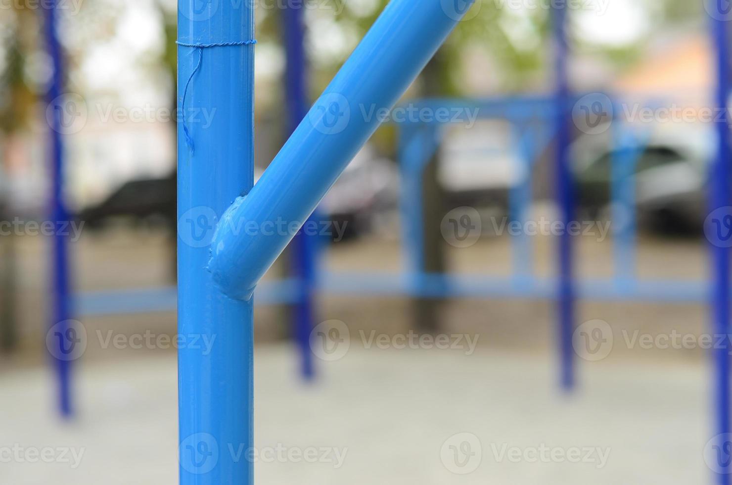 Blue metal pipes and cross-bars against a street sports field for training in athletics. Outdoor athletic gym equipment. Macro photo with selective focus and extremely blurred background
