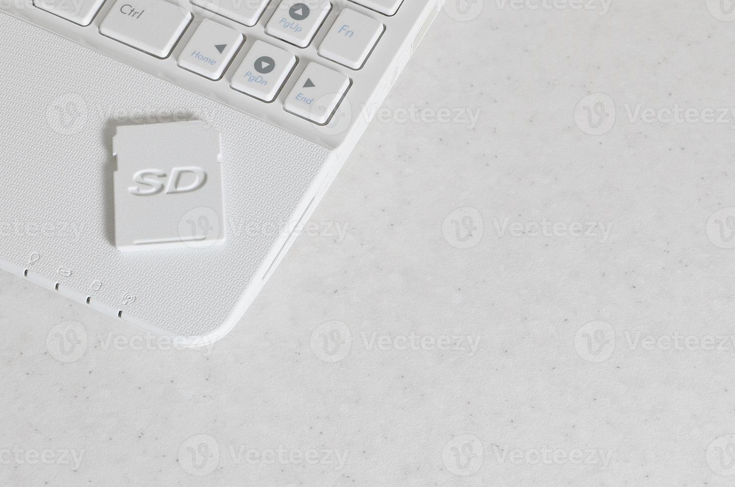 A compact SD memory card lies on a white netbook. The digital information storage device is ready for use. Concept of modern technologies photo