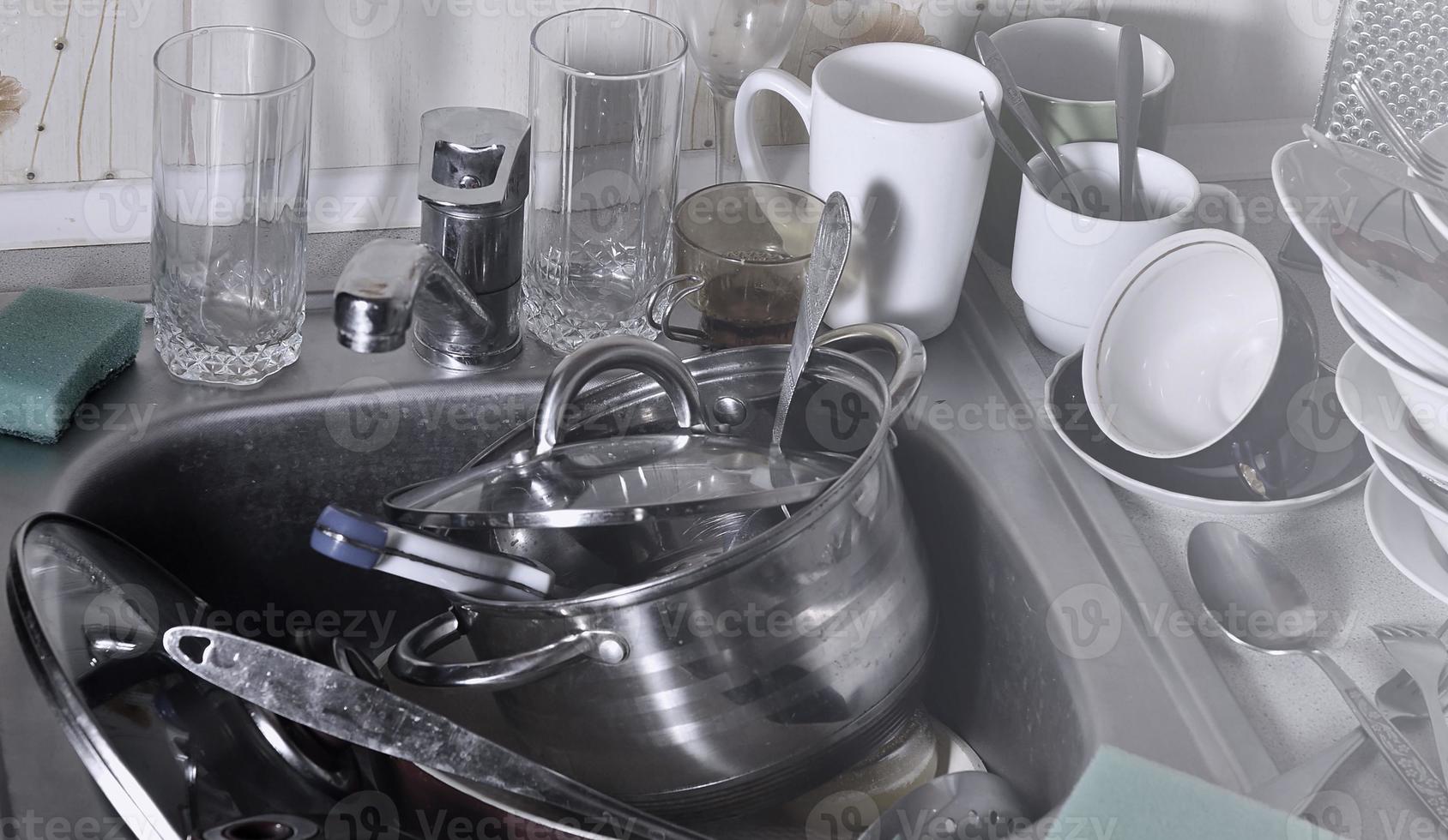 A huge pile of unwashed dishes in the kitchen sink and on the countertop photo