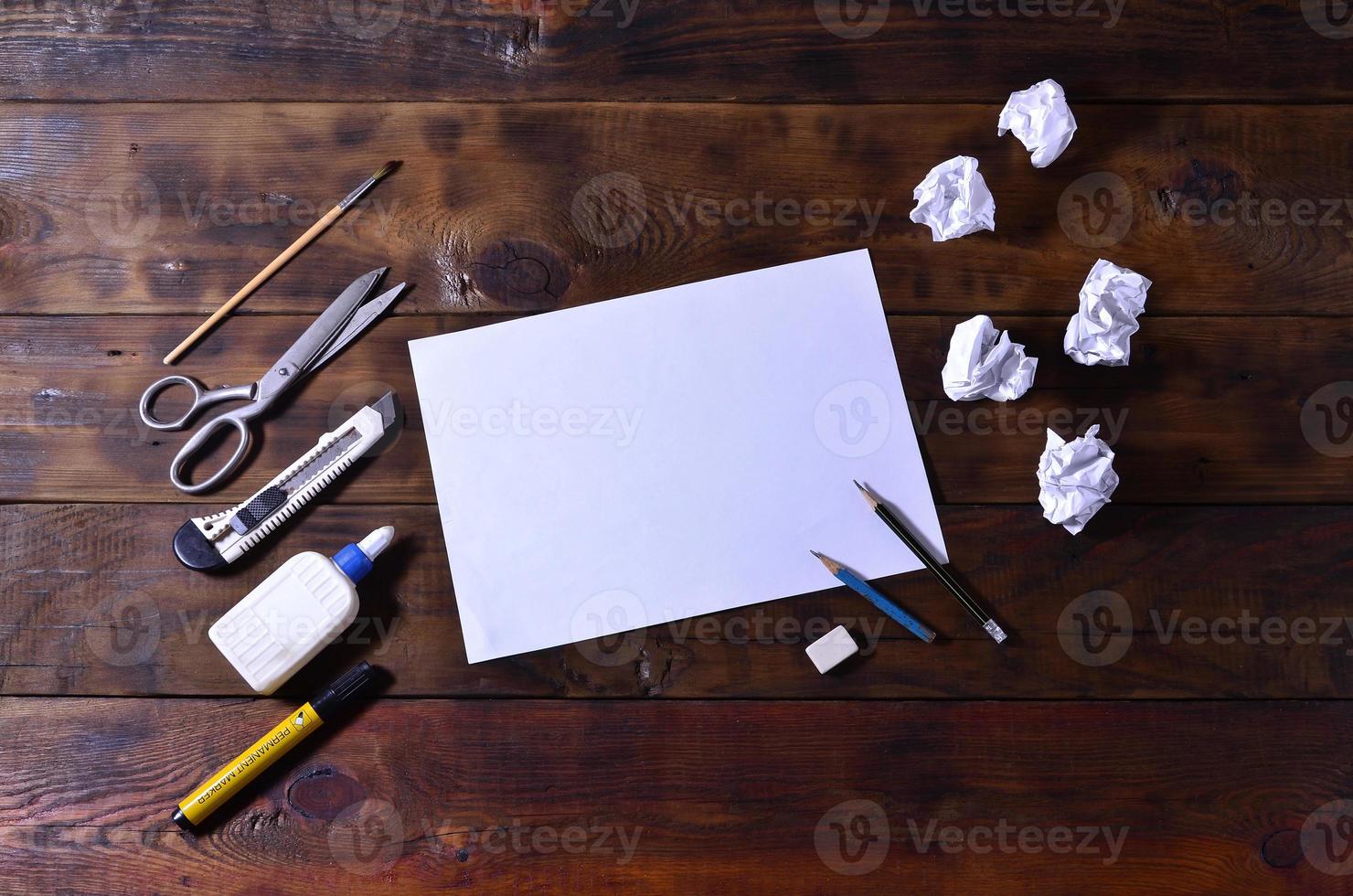 A school or office still life with a white blank sheet of paper and many office supplies. The school supplies lie on a brown wooden background. Place for text photo