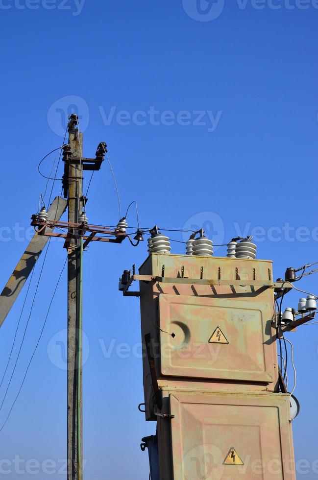 Old and obsolete electrical transformer against the background of a cloudless blue sky. Device for distribution of supply of high-voltage energy photo