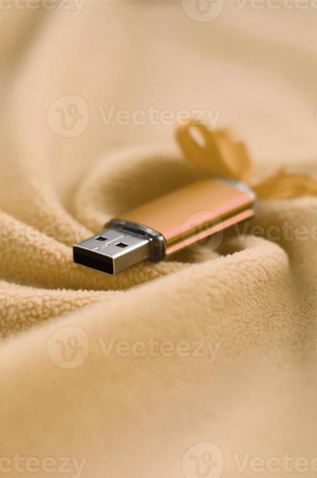 la tarjeta de memoria flash usb naranja con un lazo se encuentra sobre una manta de tela suave y peluda de color naranja claro con muchos pliegues en relieve. dispositivo de almacenamiento de memoria en diseño de mujer foto