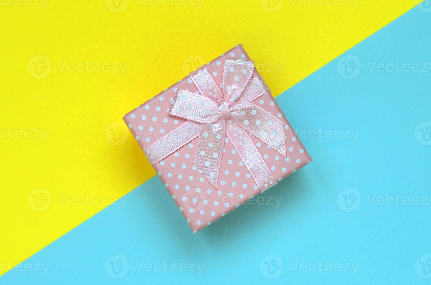 Small pink gift box lie on texture background of fashion pastel blue and yellow colors paper in minimal concept photo