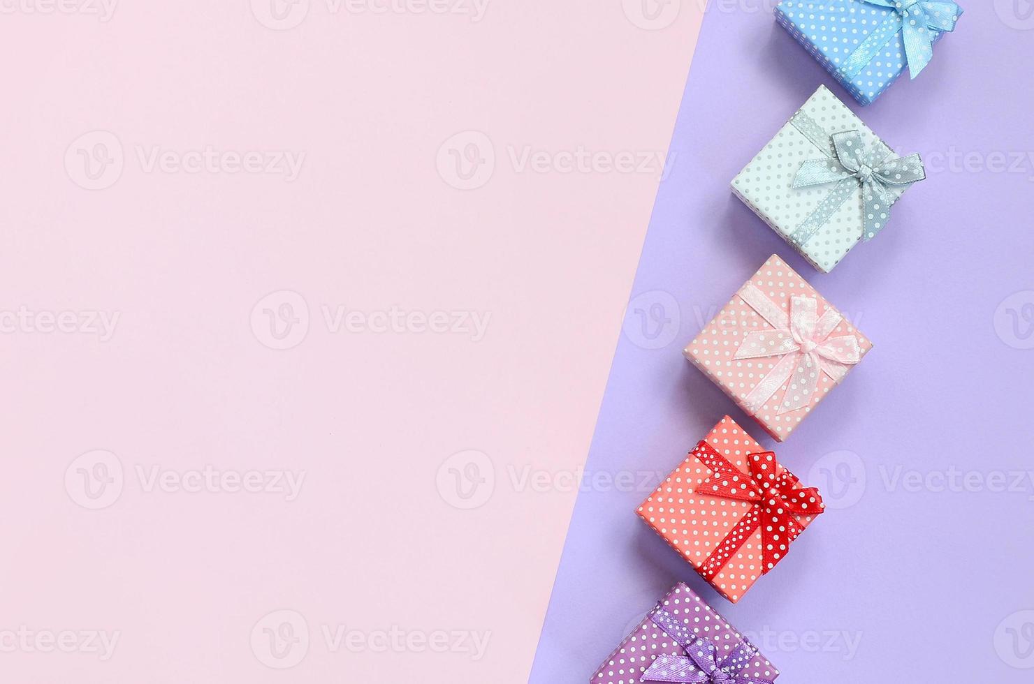 Small gift boxes of different colors with ribbons lies on a violet and pink color background photo