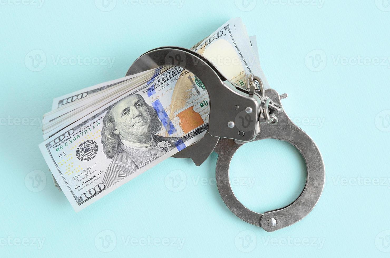 Silver police handcuffs and hundred dollar bills lies on light blue background photo