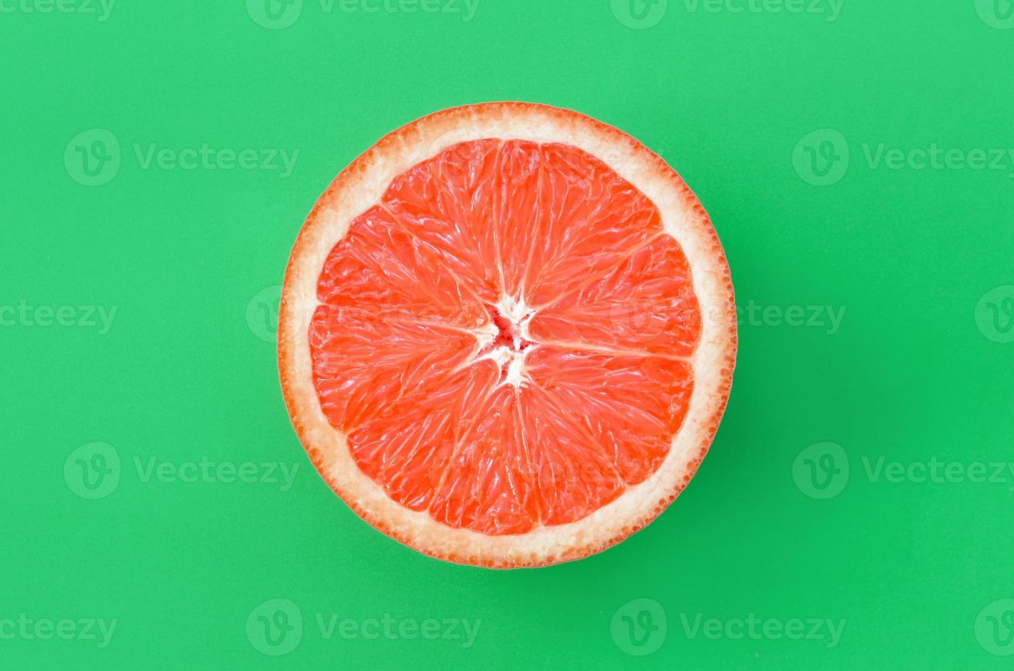 Top view of an one grapefruit slice on bright background in green color. A saturated citrus texture image photo
